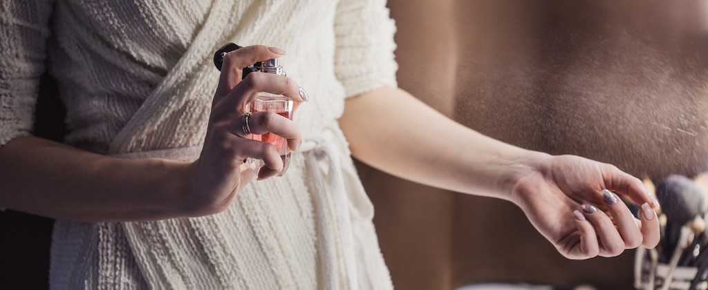 Beautiful young woman uses bottle of perfume at home, closeup