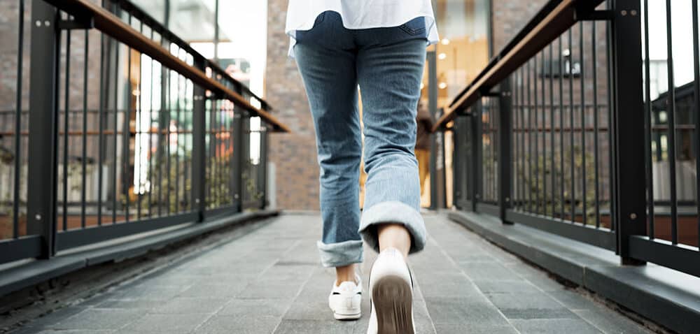 Back view of a woman in jeans and sneakers walking in the street