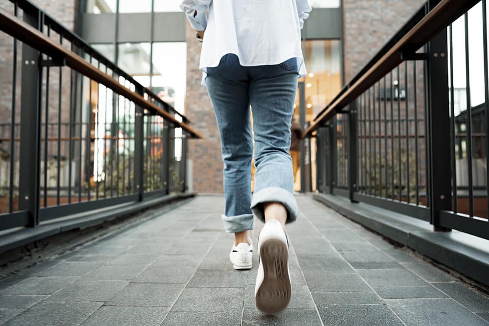 Back view of a woman in jeans and sneakers walking in the street